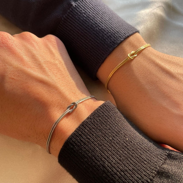 Gold and silver armbands with knot charms on wrists front view